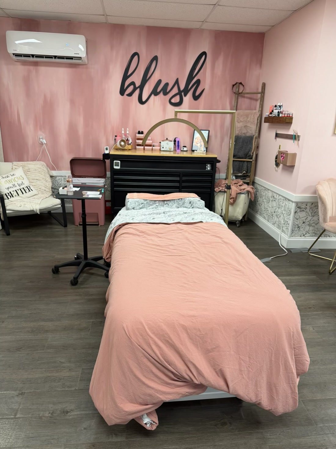 The lash room: a made-up bed under the blush sign on a soft pink wall.